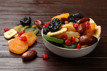 Mix of different dried fruits in bowl on wooden table, closeup