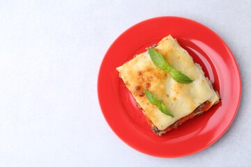 Piece of delicious cooked lasagna with basil on light table, top view. Space for text