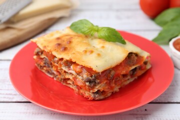 Piece of delicious cooked lasagna with basil on light wooden table, closeup