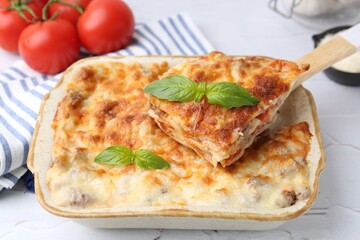Delicious cooked lasagna with basil in baking dish on white textured table, closeup