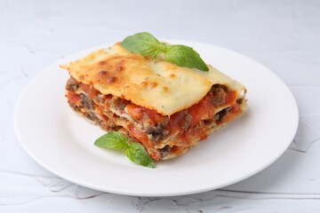 Piece of delicious cooked lasagna with basil on white textured table, closeup