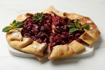 Tasty galette with cherries and mint on white marble table