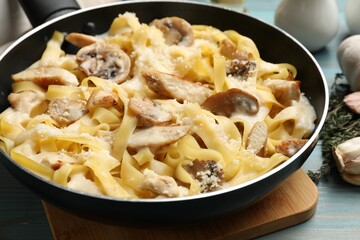Tasty Alfredo pasta with chicken and mushrooms in frying pan on light blue wooden table, closeup