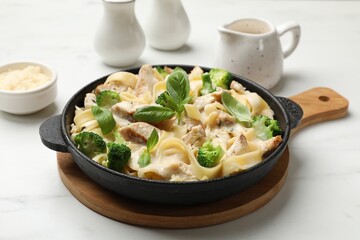 Delicious pasta Alfredo with chicken, cheese, creamy sauce, broccoli and basil on white marble table, closeup
