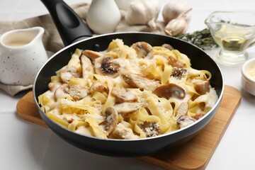 Tasty Alfredo pasta with chicken and mushrooms in frying pan on light table, closeup