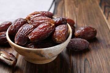 Many tasty dried dates in bowl on wooden table, closeup