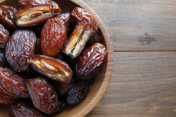 Many tasty dried dates in bowl on wooden table, top view. Space for text