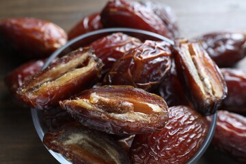 Many tasty dried dates in bowl on brown table, closeup