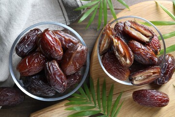 Many tasty dried dates in bowls and leaves on wooden table, flat lay