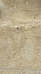 Close-up of a beige textured stone wall, showcasing its rough surface, natural imperfections, and timeless appeal, perfect for architectural or background design concepts.

