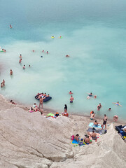 Many people swimming in the blue water near the sandy shore in a flooded quarry on a summer day. Beautiful blue water of large lake and many people swimming near the sandy shore of the slope. Top view