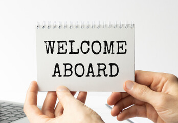 Businesswoman hands holding white card sign with welcome aboard text message isolated on grey wall office background. Retro instagram style image