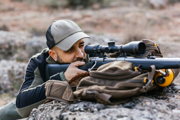 Hunter aiming with rifle lying on rocks in the mountain