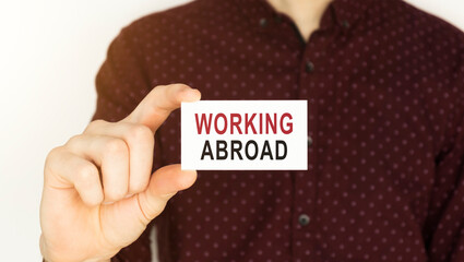 Businessman holding a card with text WORKING ABROAD.
