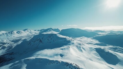 Obraz premium Drone view of mountains covered in the snow under the sunlight and a blue sky