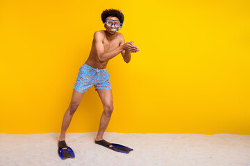 Young man wearing snorkeling gear and shorts poses playfully against a vibrant yellow background, embodying summer fun.