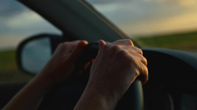 Traveling through countryside by your own car, closeup of female hands gripping the steering wheel of a modern automobile vehicle, 4K