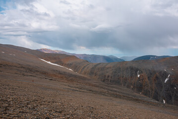 Dramatic awesome top view from pass above large sharp ridge to alpine deep valley among big cliffs far away in rain under gray cloudy sky. High rocky mountain silhouettes on horizon in rainy clouds.