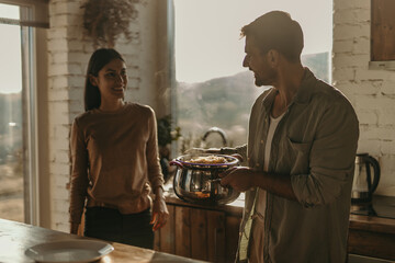 A loving couple laughing while serving pasta for lunch in a sunny kitchen