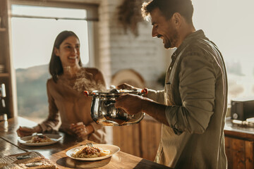 Cheerful scene of a couple sharing pasta at their sunny kitchen table