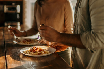 Cheerful scene of a couple sharing pasta at their sunny kitchen table