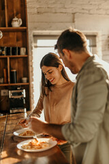 Couple enjoying spaghetti in a kitchen bathed in sunlight. Laughter and good food
