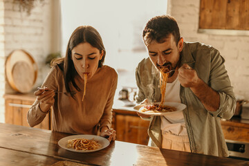 Man and woman eating pasta together in a vibrant, well-lit home