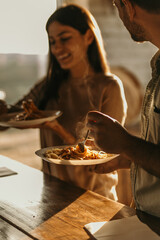 Joyful couple sharing a pasta meal in their sunny kitchen with natural light streaming in