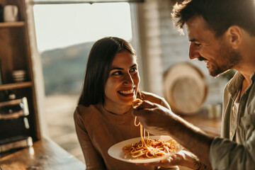 Smiling man and woman sharing a meal of pasta in their modern, sunny home