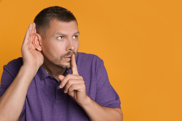 Man showing hand to ear gesture on orange background, space for text