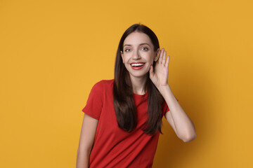 Woman showing hand to ear gesture on orange background