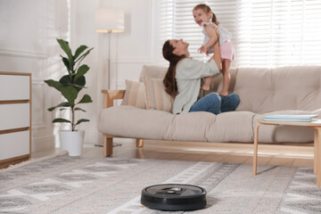 Mother spending time with her daughter in room, focus on robotic vacuum cleaner