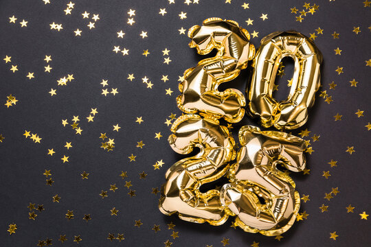 New year 2025 balloon celebration card. Gold foil helium balloon number 2025, party decoration, gold confetti stars on black background. Copy space, flat lay, merry christmas, happy holidays concept.