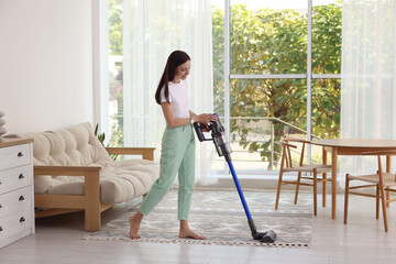 Smiling young woman cleaning floor with cordless vacuum cleaner at home