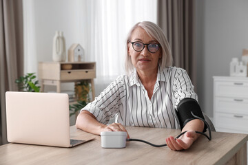 Woman measuring blood pressure at wooden table indoors