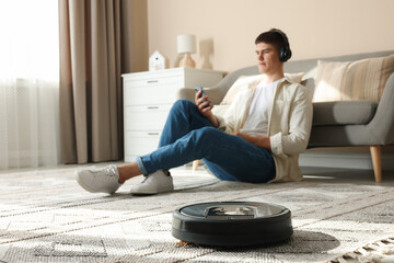 Robotic vacuum cleaner cleaning carpet while man relaxing at home