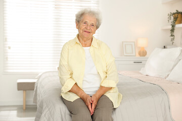 Beautiful senior woman sitting on bed at home