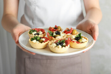 Woman holding plate with tasty canapes on light grey background, closeup