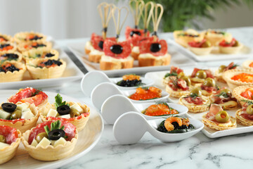 Many different tasty canapes on white marble table, closeup