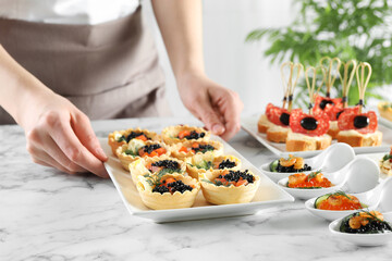 Woman with many different tasty canapes at white marble table, closeup