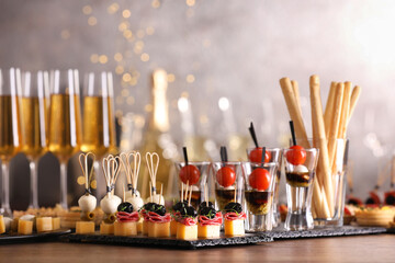 Many different tasty canapes and wine on wooden table against blurred lights