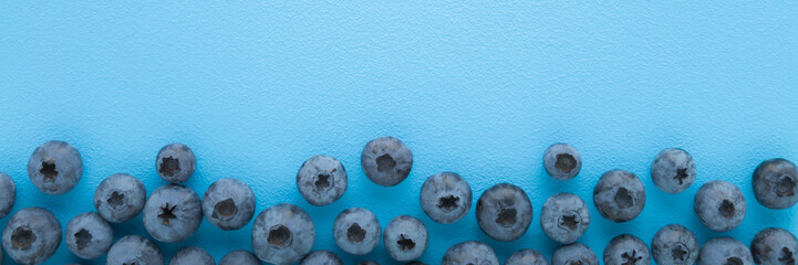 Fresh blueberries on light blue table background. Pastel color. Closeup. Wide banner. Empty place for text. Top down view.