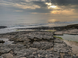 Obraz premium Rocky shoreline with gentle waves and tide pools at sunset on UK coast