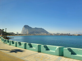Gibraltar rock overseeing the seafront promenade with palm trees and benches on a sunny summer day