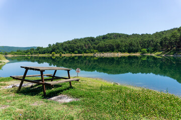 Idyllic Wooden Bench next to Tranquil Lakeside. Peaceful Picnic Spot by the Lake with Nature Reflections. Green Scenery with selective focus