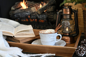Hot chocolate by a fireplace with books and lantern - cozy winter background