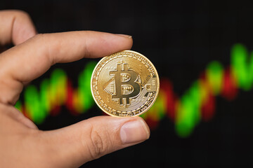 Hand holding a finance coin in front of a stock market chart