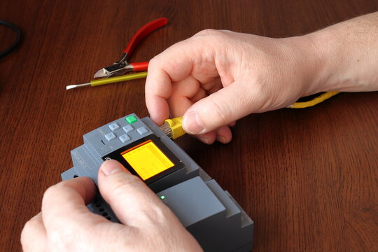 Close-up of a hand connecting a mini industrial PLC to a network. Testing and programming of an industrial control system.