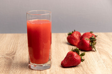un vaso con jugo rojo al fondo un grupo de frutillas desenfocadas