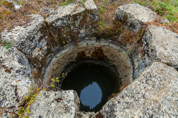 Obraz premium An ancient stone well, partially filled with water, surrounded by lush vegetation